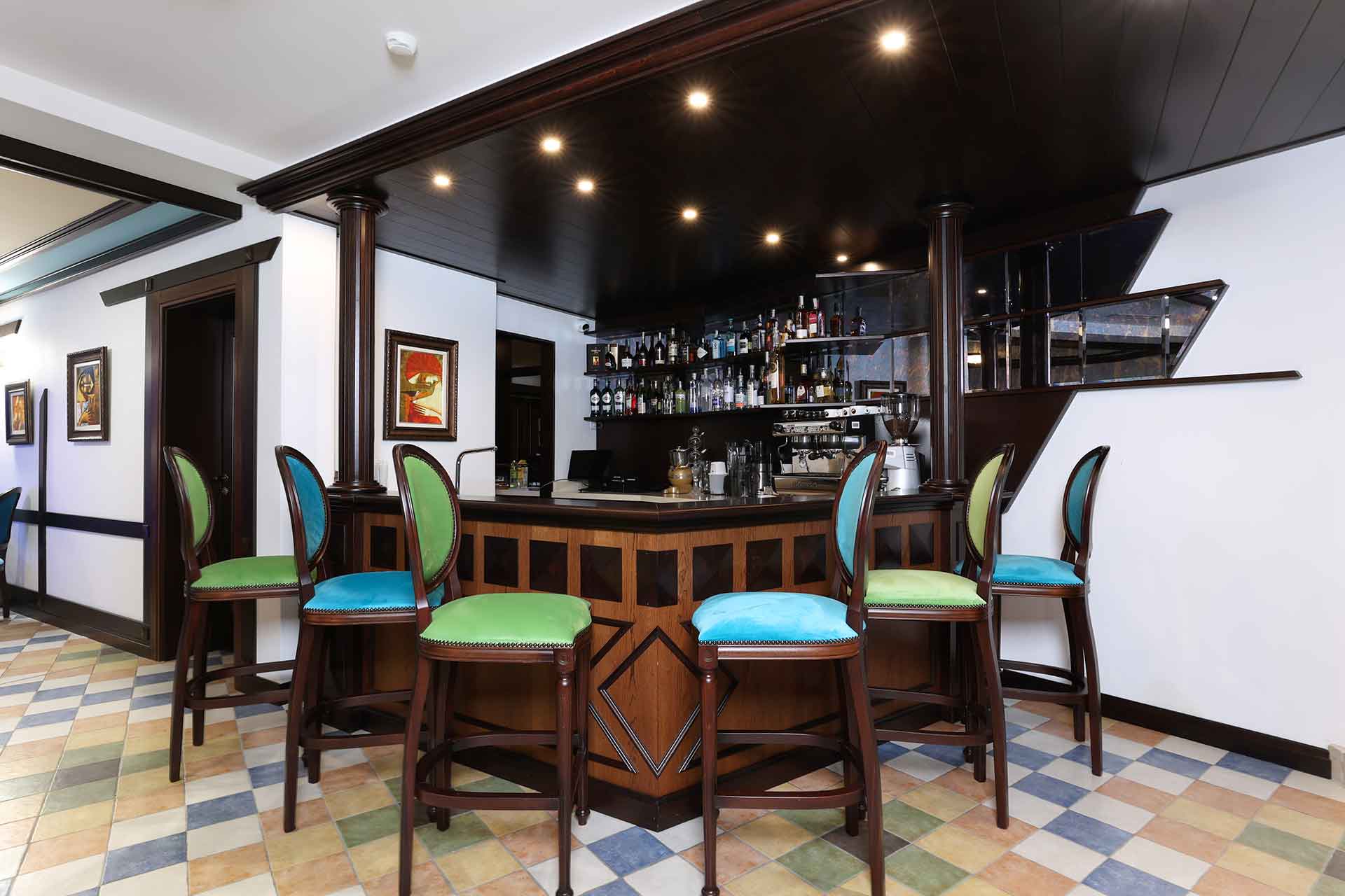 Lobby bar of Armaco Resdience. Bar with two shelfs with alcohol, six green and blue bar chairs .